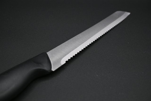 An image of a bread knife with a focus on the blade, displayed diagonally against a black background.