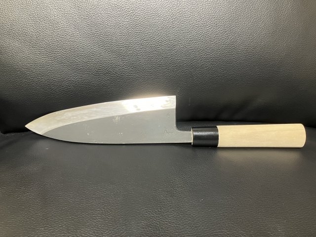 An image of a Deba knife standing upright with its blade facing upwards against a black background.