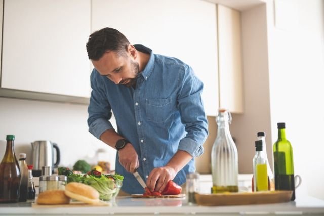 A man slicing a vegetable in a kitchen at home