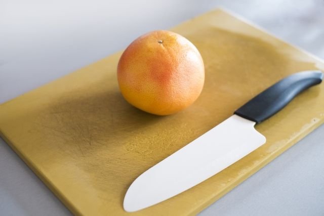 A ceramic kitchen knife on a chopping board with an orange