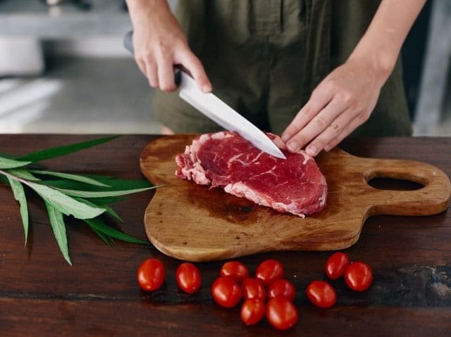 A person cutting meat on a chopping board with a kitchen knife