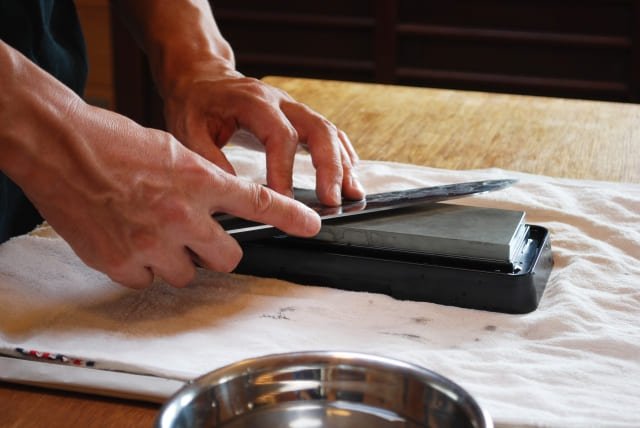 Close-up of hands using a whetstone to sharpen a kitchen knife.