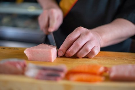 Focused image of a Japanese chef is slicing fish neatly and making sashimi