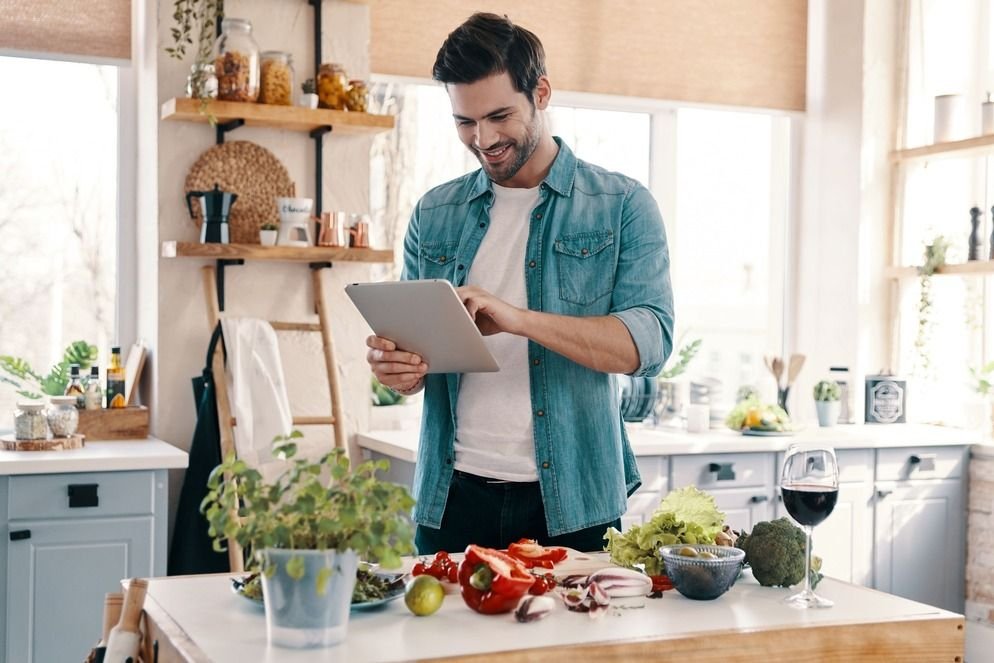 a man using a tablet while cutting vegetables in the kitchen