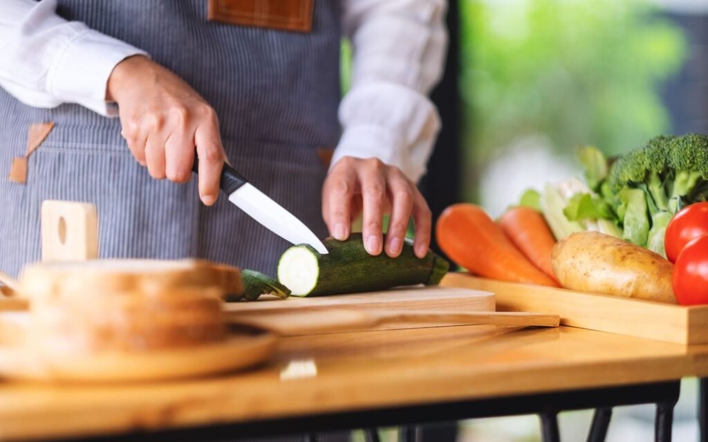 a woman slicing a courgette on a wooden chopping board