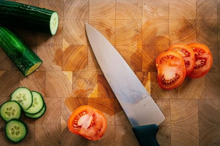 Sliced cucumber and tomato with kitchen knife placed diagonally on cutting board
