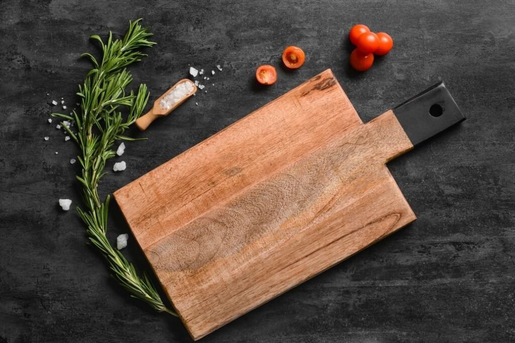 Wooden cutting board with a tomato, fresh herbs, and salt on a black background