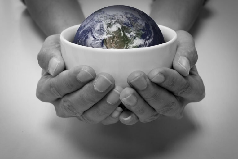 Hands holding a transparent Earth on a green field, expressing environmental awareness