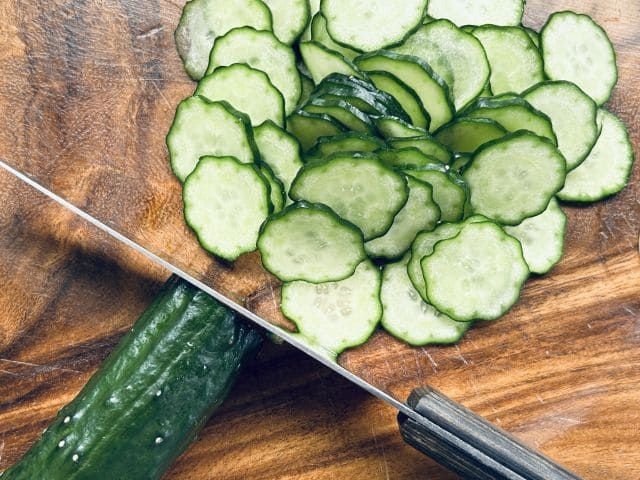 Slices of cucumbers on a chopping board with a kitchen knife