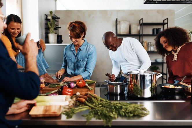 A woman cooking dinner surrounded by smiling friends